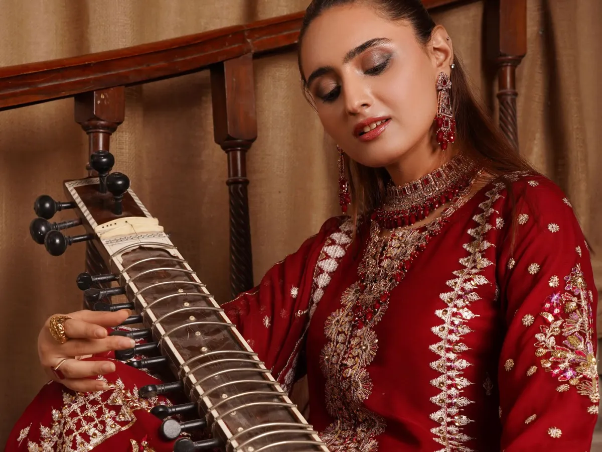 A musician in red and gold traditional dress playing a sitar, hands on the strings