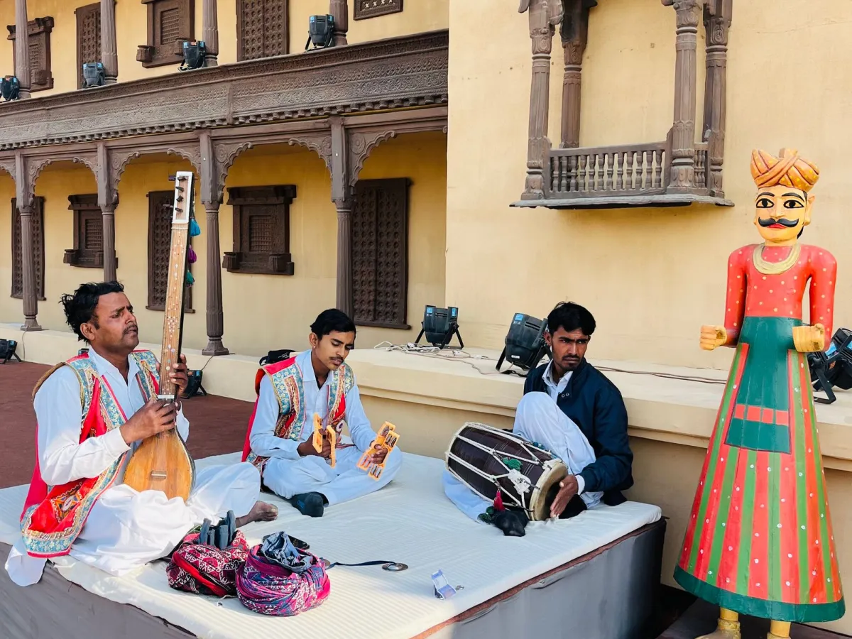 Folk musicians with tanpura, khartal and dholak performing on a low platform outside a carved haveli
