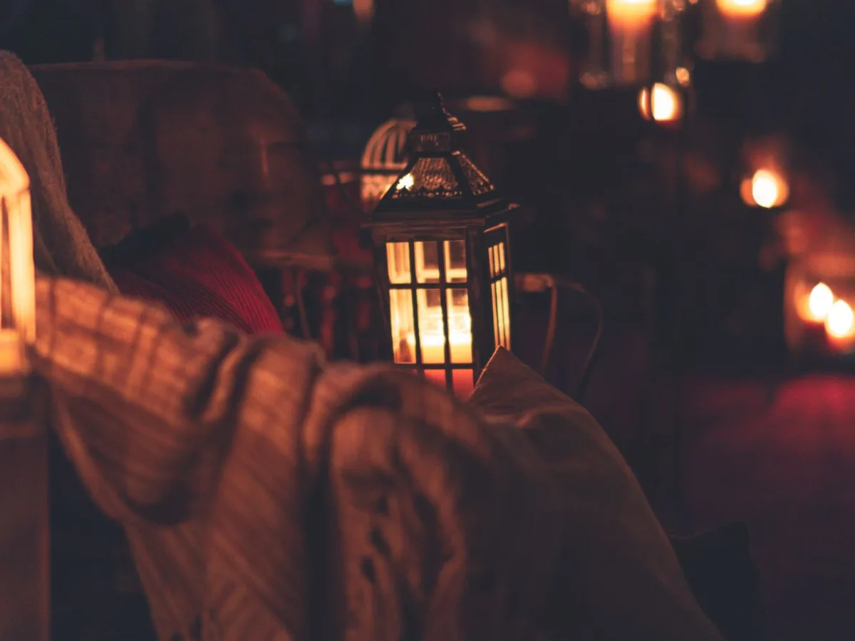 A lantern glowing among soft throws and candlelight as a room is readied for guests