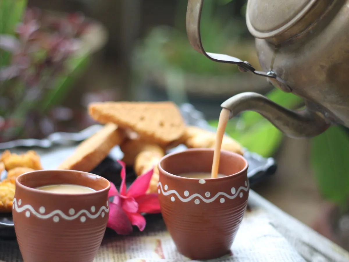 Milky tea poured into clay cups alongside light snacks, set out for arriving guests